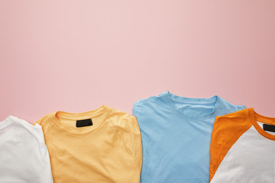 top view of folded color t-shirts on pink background