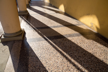 Arched passageway (arcade) in Bologna, Italy: columns are casting long shadows on terrazzo floor...