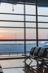 Obraz premium View of airport interoir, empty bench chairs in the departure hall during sunrise. Airplane and building background. Travel and transportation concept