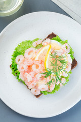 Traditional savory swedish sandwich with a dark bread, lettuce, eggs, mayonnaise, shrimps, dill and lemon, vertical,  top view
