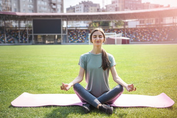Woman training outdoors. She's sitting on mat on green grass and doing yoga exercises