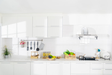 Modern white kitchen with counter and white details, minimalist interior, Full set of kitchen equipment, pan, pot, electric hob, flipper, vegetable, fruit.