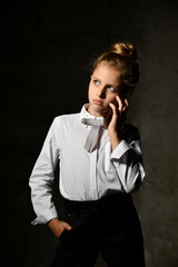 Little female caucasian model posing in school uniform on a gray concrete studio background.