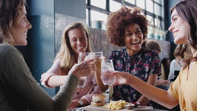 Four Young Female Friends Meeting For Drinks And Food Making A Toast In Restaurant