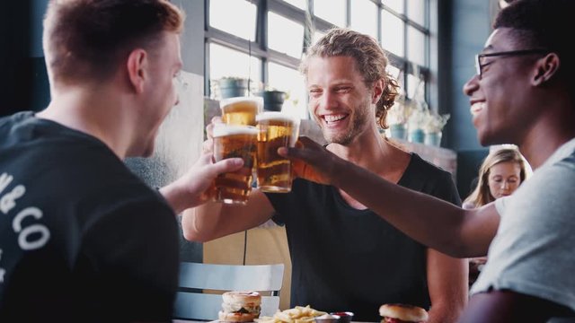 Three Young Male Friends Meeting For Drinks And Food Making A Toast In Restaurant