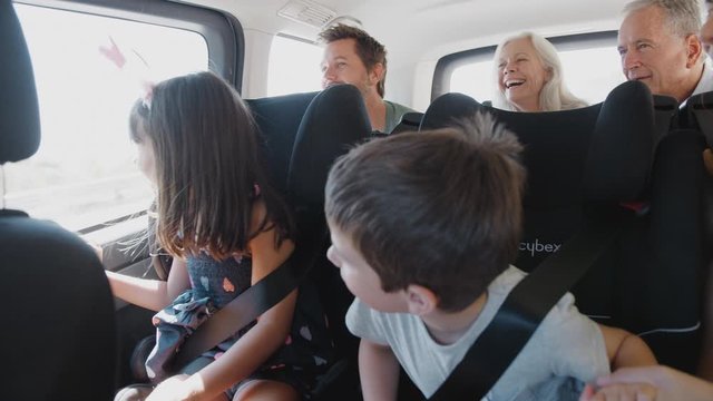 Multi Generation Family Sitting In Back Of People Carrier Being Driven To Vacation