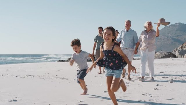 Multi Generation Family Walking Along Sandy Beach On Summer Vacation