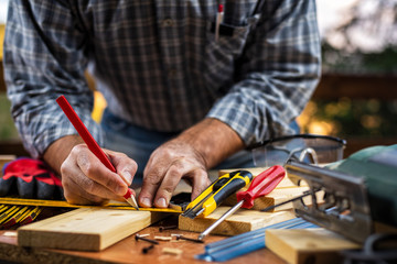 Fototapeta na wymiar Adult carpenter craftsman with a pencil and the carpenter's square trace the cutting line on a wooden table. Construction industry, housework do it yourself. Stock photography.