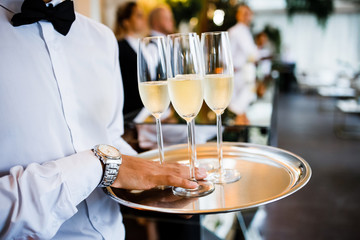 The waiter is holding a tray with glasses of refreshing champagne