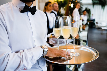 The waiter is holding a tray with glasses of refreshing champagne