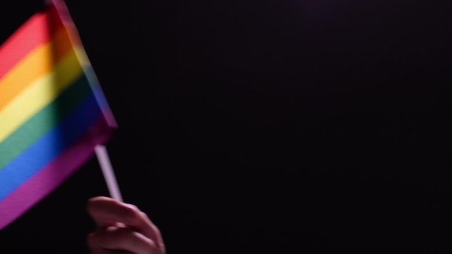 Male hand waving a rainbow flag. Black background. LGBT concept. Advocacy of sexual independence and freedom of relationship and love.
