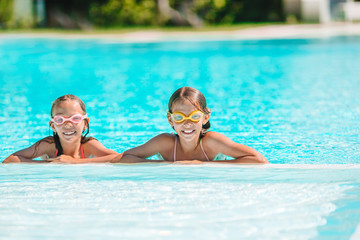 Fototapeta premium Adorable little girls playing in outdoor swimming pool on vacation