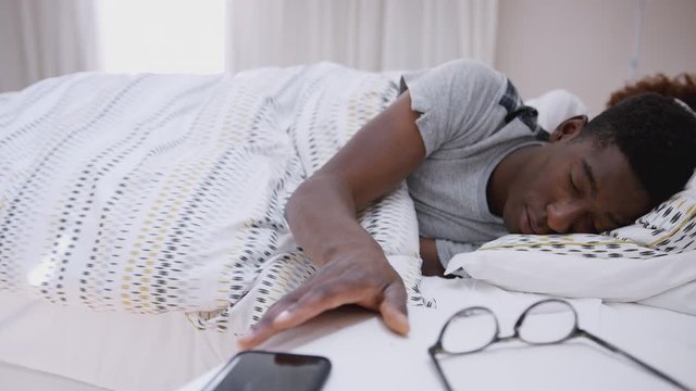 Man Asleep In Bed Reaches Out To Turn Off Alarm On Mobile Phone
