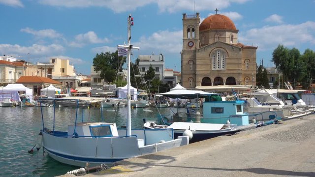 Fshing boats and waterfront with Ekklisia Isodia Theotokou Church on sunny summer day in Aegina town, Saronic Islands, Greece
