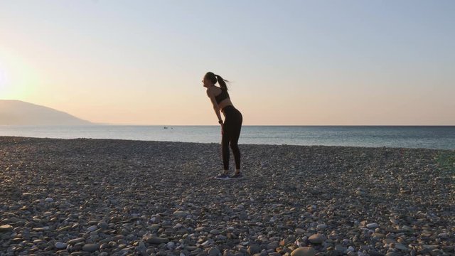 A young female runner runs at sunrise along the promenade, then stops to rest. Woman resting after jogging on the beach.