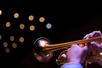 A trumpet player playing on a gold plated matte lacquered trumpet during a performance with bokeh...