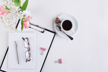 Female workspace with a tablet, ballpoint pen, glasses, flowers and a cup of black coffee. view from above