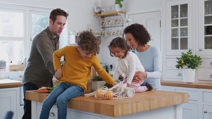 Family Returning Home From Shopping Trip Using Plastic Free Bags Unpacking Groceries In Kitchen