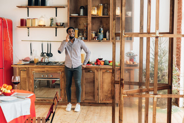 Young black man talking on mobile phone in kitchen