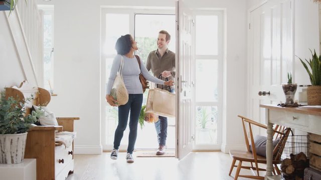 Couple Returning Home From Shopping Trip Carrying Groceries In Plastic Free Bags