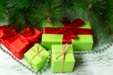 Colored gifts with wrapped bows lie under a Christmas tree on a wooden floor