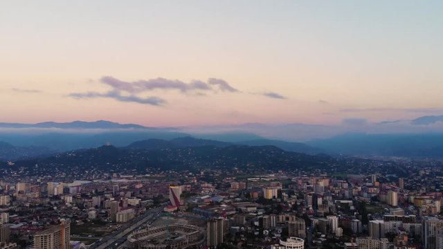 Aerial flying rise above the city center of Batumi, Georgia. In the background mountain covered with a small evening haze and clouds. Taken by drone after sunset