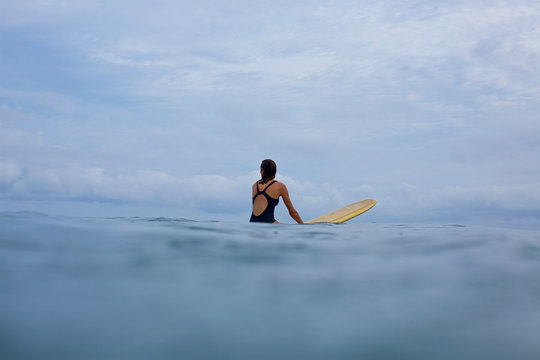 Female surfer straddling surfboard in ocean