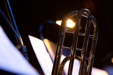 A part of a shiny trombone is being backlit by a light that is attached to a music stand