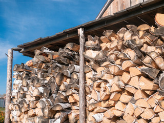 Firewood stacked in a woodpile under a wooden canopy in the open air under the blue sky.