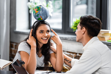 bi-racial student pointing with fingers at globe and smiling with friend