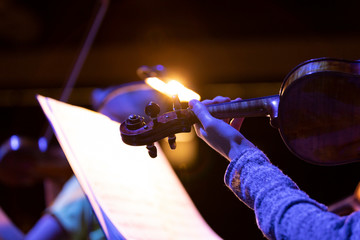A musician with playing a violin with a bow and a music stand with it light shining bright in the background