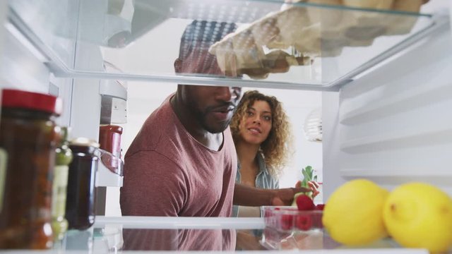 View Looking Out From Inside Of Refrigerator As Couple Open Door And Unpacks Shopping Bag Of Food