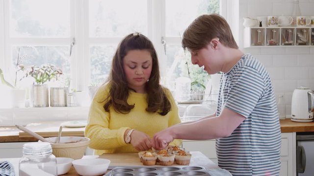 Young Downs Syndrome Couple Taking Homemade Cupcakes Out Of Baking Tray