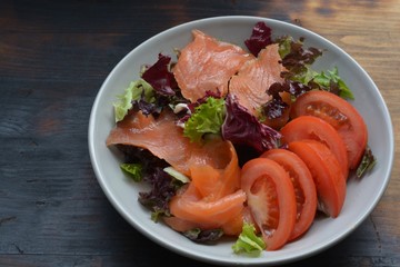 Salmon salad in a bowl with tomatoes on a burned table background