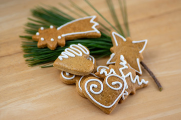 Painted traditional Christmas gingerbreads arranged on wooden background in daylight, common tasty sweets on pine branch needles