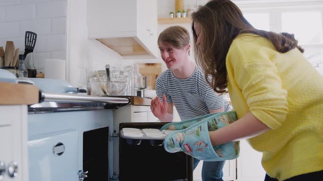 Young Downs Syndrome Couple Putting Homemade Cupcakes Into Oven In Kitchen At Home