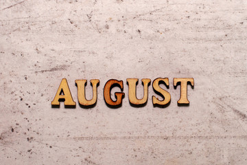 The word August laid out in wooden letters on a light background. Close-up. Summer time years and months of the year.