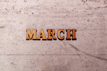 The word March laid out in wooden letters on a light background. Close-up. Summer time years and months of the year.