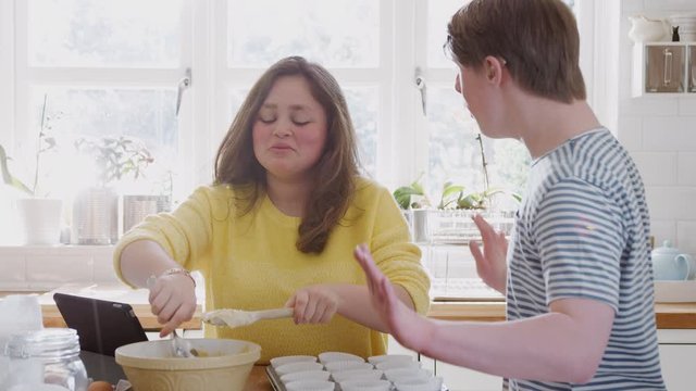 Young Downs Syndrome Couple Putting Mixture Into Paper Cupcake Cases In Kitchen At Home