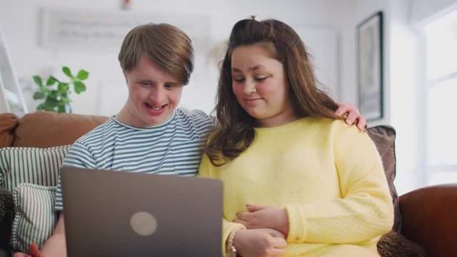 Young Downs Syndrome Couple Sitting On Sofa Using Laptop At Home