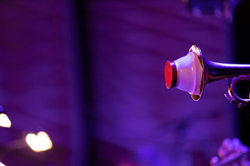 A trumpet bell with a cup mute during a live performace of a big band concert with purple stage lights as well as some warm light coming from the music stand lights