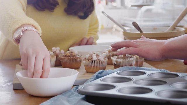 Close Up Of Downs Syndrome Couple Decorating Homemade Cupcakes With Marshmallows In Kitchen At Home