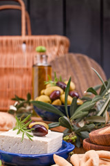 Obraz na płótnie Canvas Greek cheese feta with thyme and olives, selective focus. Bread and young olives branch on olive board over old wood background. Overhead view.