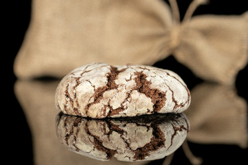One whole baked chocolate brownie cookie with jute bag isolated on black glass