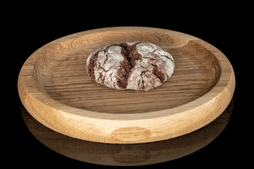 One whole baked chocolate brownie cookie on bamboo plate isolated on black glass