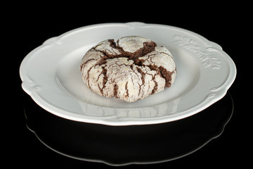 One whole baked chocolate brownie cookie on white plate isolated on black glass