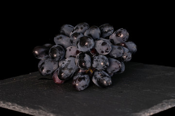 Lot of whole fresh black grape on grey stone isolated on black glass