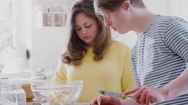 Young Downs Syndrome Couple Adding Butter To Cake Recipe They Are Baking In Kitchen At Home