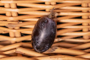 One whole fresh black grape with braided rattan behind
