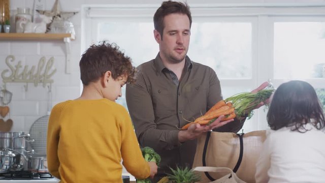Family Returning Home From Shopping Trip Using Plastic Free Bags Unpacking Groceries In Kitchen